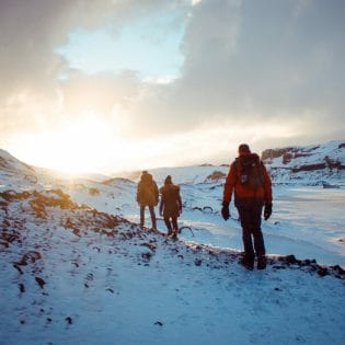 Arctic hikers walking over snowy terrain towards a sunset.
