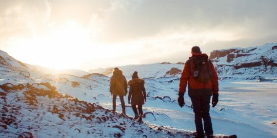 Arctic hikers walking over snowy terrain towards a sunset in search of the January 2023 newsletter
